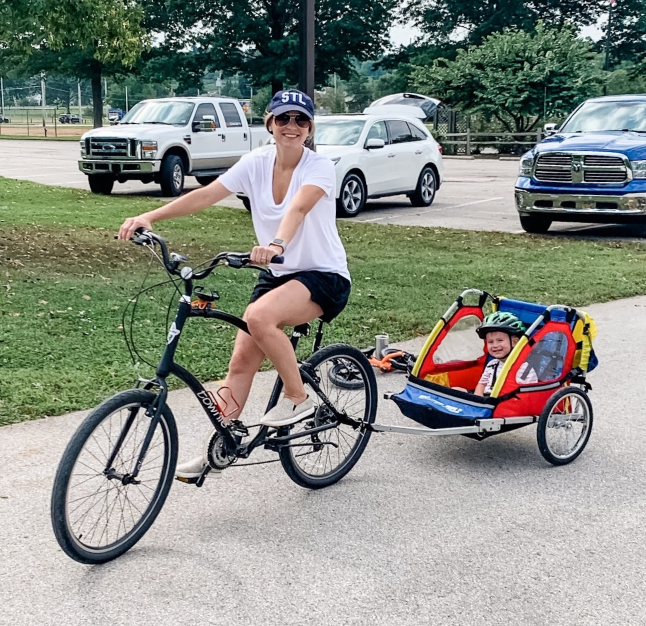 PAH patient, Chelsea, wearing a white shirt and black shorts while bike riding and pulling her son in a bike trailer