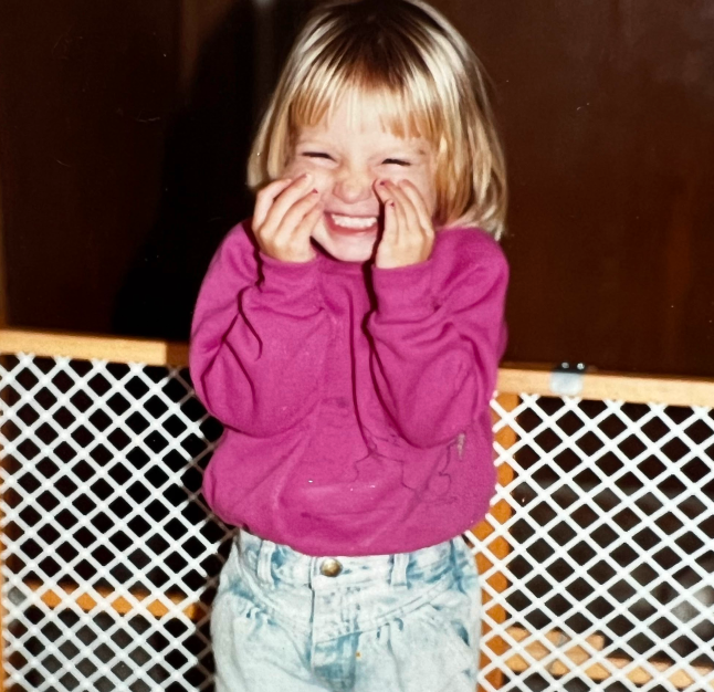 PAH patient, Chelsea, as a little girl wearing a pink sweater and jeans smiling broadly