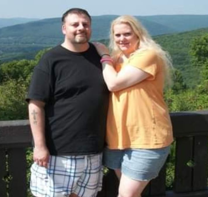 PAH patient, Rochelle, and her male caregiver, Tim, standing in front of tree-lined mountains