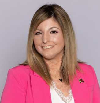Scleroderma and PAH patient, Amy, smiling warmly in front of a grey backdrop wearing a bright pink blazer and white shirt