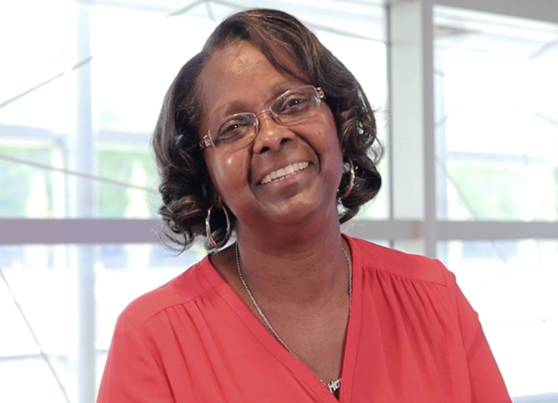 Female PAH patient, Nola, wearing glasses and a red shirt smiling in front of a window