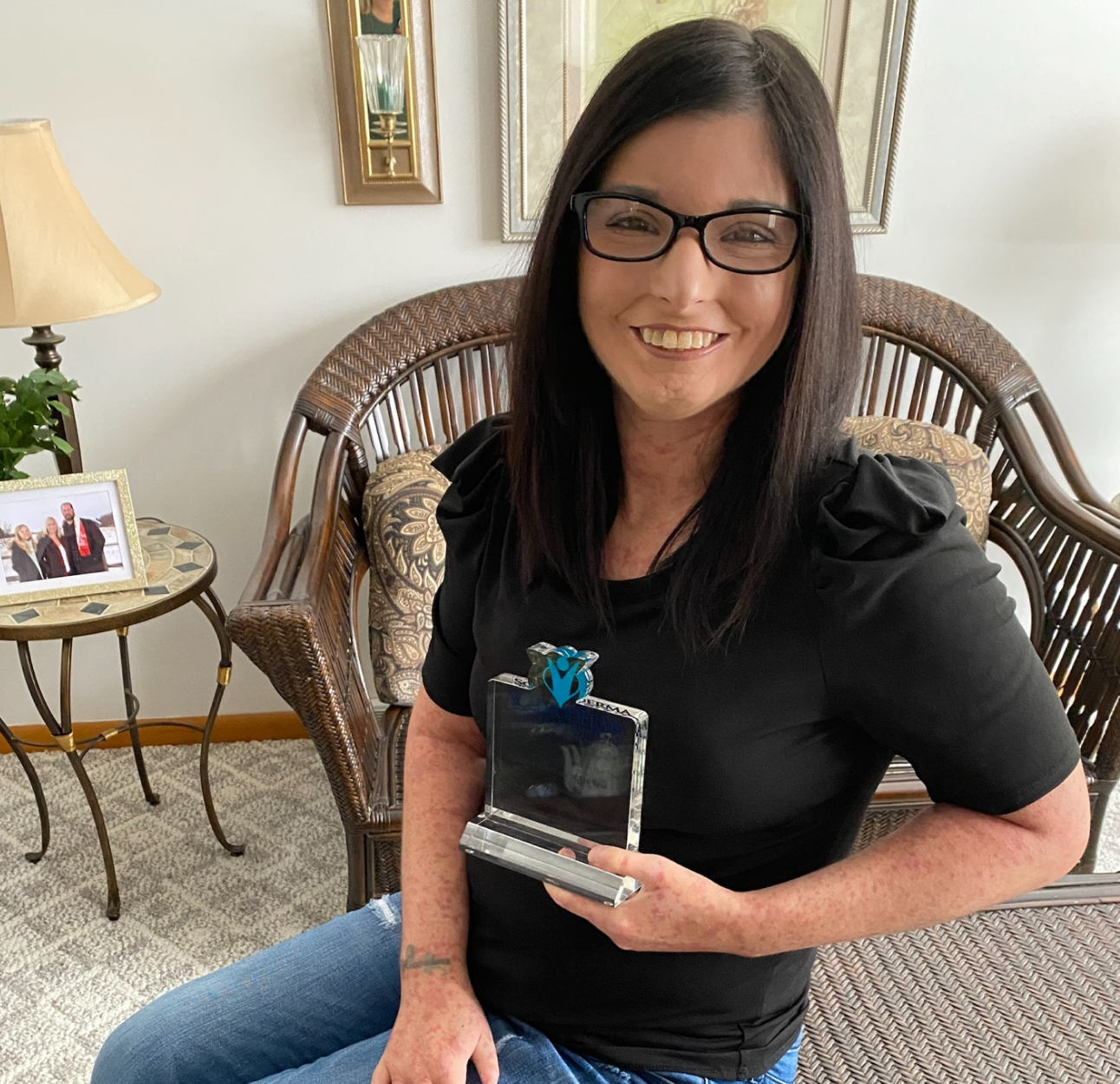 Scleroderma and PAH patient, Amy, wearing glasses and a black shirt while smiling and holding an award