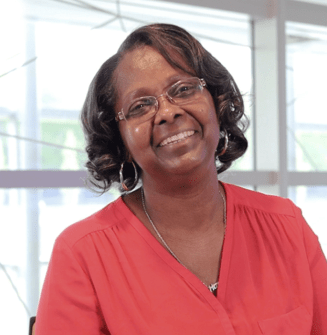 Female PAH patient, Nola, wearing glasses and a red shirt smiling in front of a window