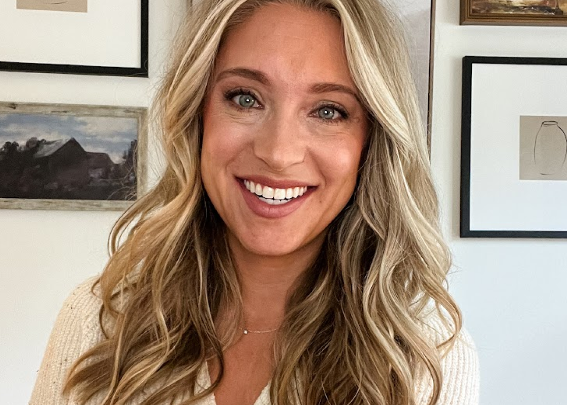 PAH patient, Chelsea, smiling in front of a wall of picture frames wearing a cream sweater