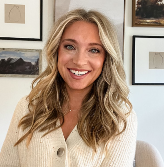 PAH patient, Chelsea, smiling in front of a wall of picture frames wearing a cream sweater 
