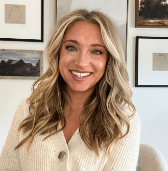 PAH patient, Chelsea, smiling in front of a wall of picture frames wearing a cream sweater 