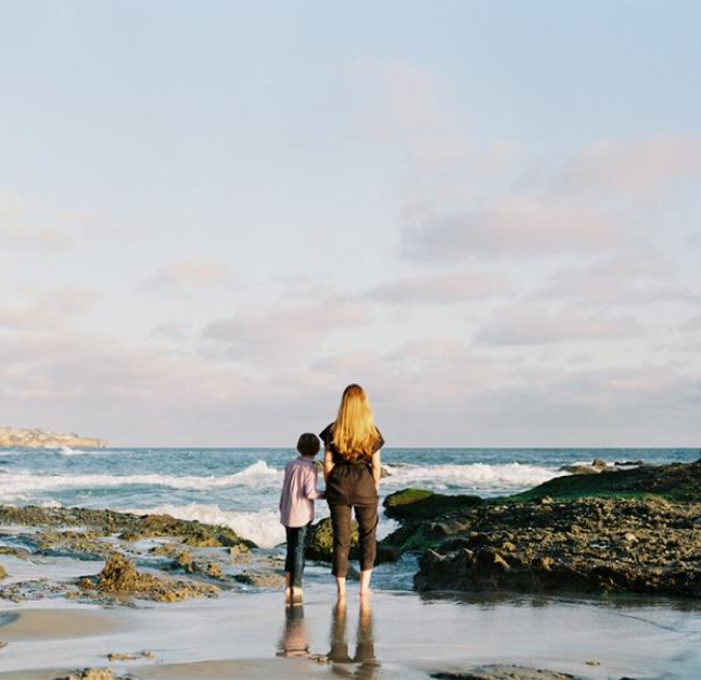 PAH patient, Katie, holding hands with her son at a rocky beach facing away from camera