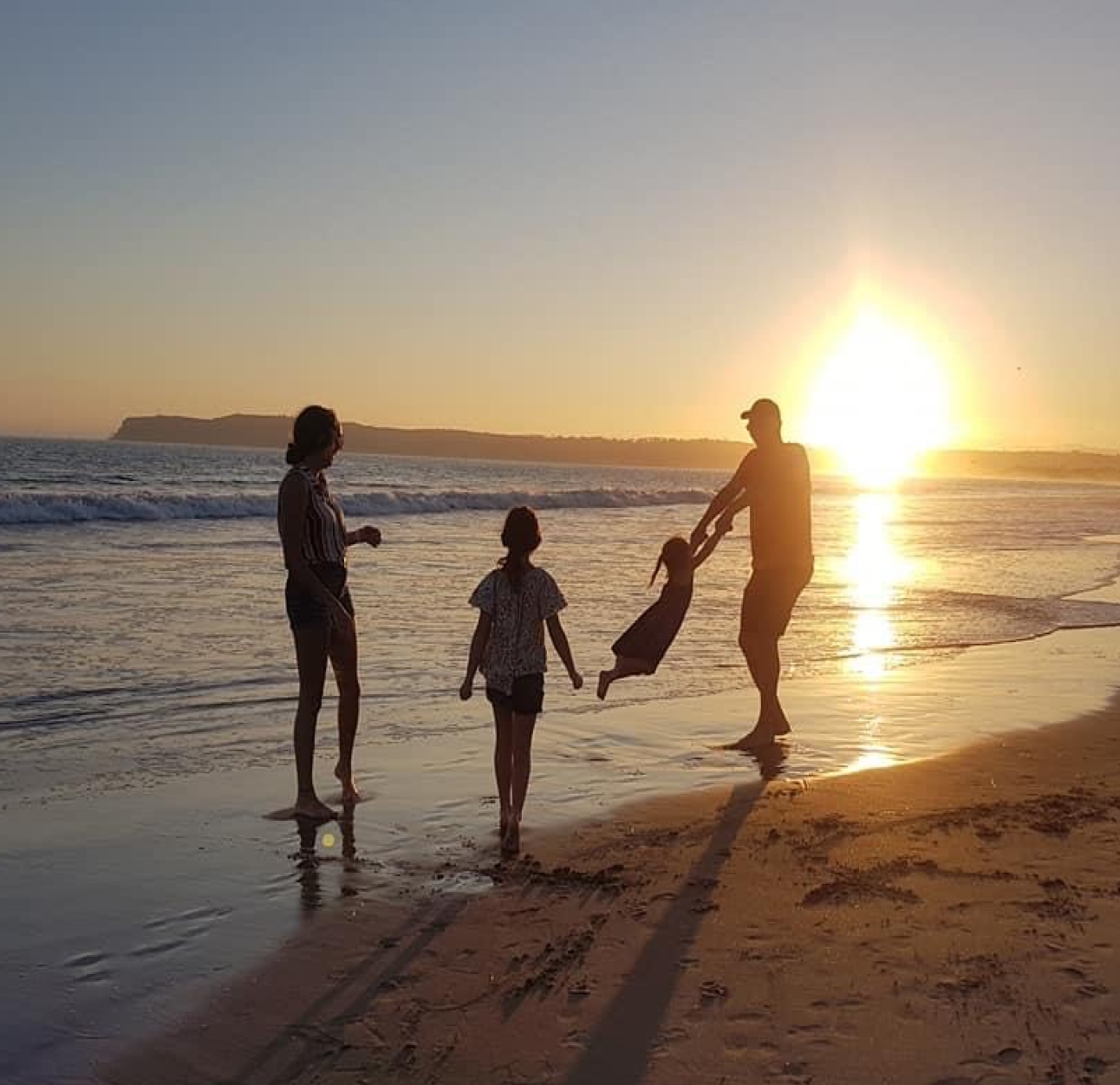 Silhouette of PAH patient, Steve, and his daughter playing with his two grandchildren at the beach at sunset