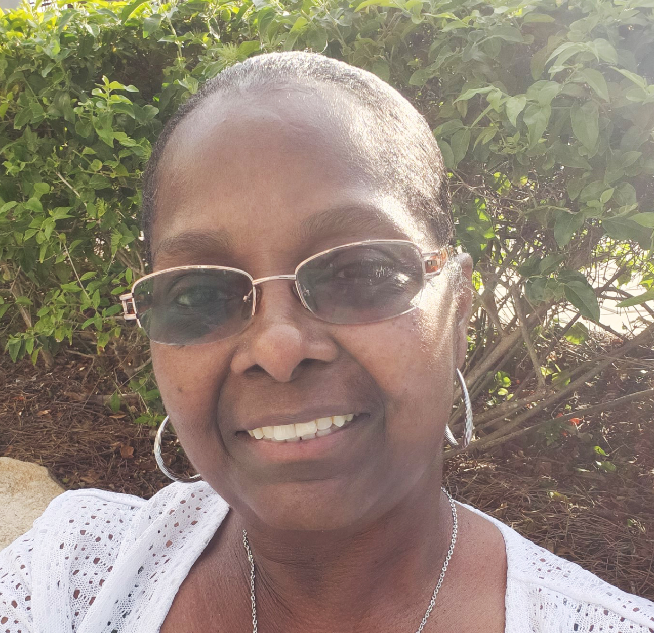 Female PAH patient, Nola, taking a selfie while wearing glasses outside in front of shrubs