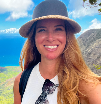 PAH patient, Katie, smiling while hiking in the mountains on a sunny day wearing a straw hat and backpack