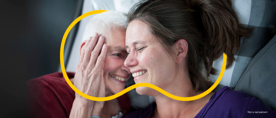 Woman holds another woman's hand to her cheek while laying together and smiling with yellow Outnumber PAH symbol around them 