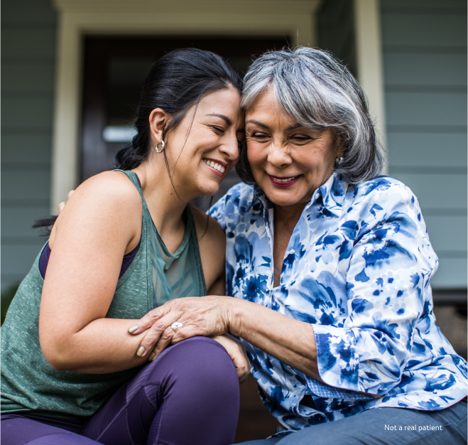 Two women laughing and embracing while sitting side by side on the front steps of a house