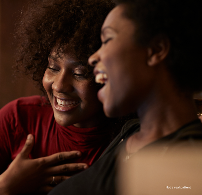 Profile view of a woman in a red shirt laughing with another woman in a black shirt