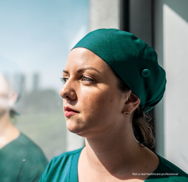 A female doctor wearing green scrubs and surgical hat looking out of a window