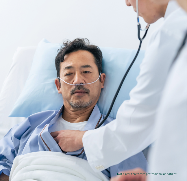 Man laying in a hospital bed wearing oxygen tubes while a doctor listens his heartbeat with a stethoscope